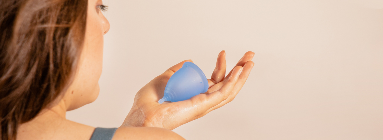 Mujer joven mostrando la copa menstrual BLOOM corta en su mano izquierda